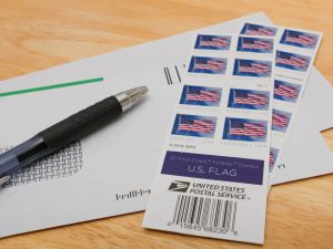 Various stams from the USPS with the U.S. Flag on them with envelopes underneath - GAINSWave